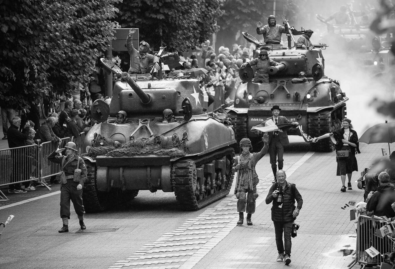 Tanks rijden over straat, met mensen erop en errond