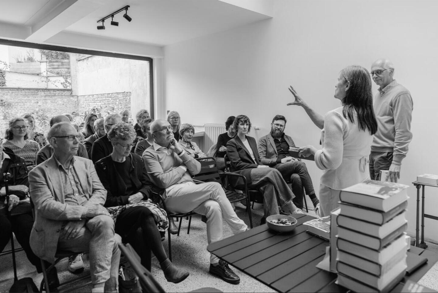 Mensen zitten en luisteren, twee mensen staan recht naar publiek gekeerd
