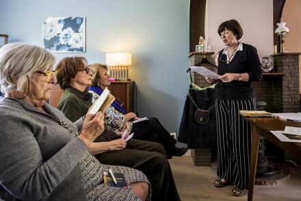 vrouw staat vooraan, voor zittende mensen