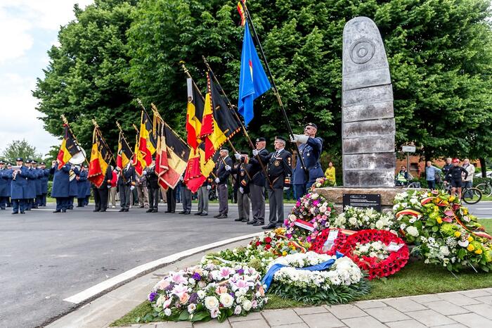 Monument met bloemenkransen en personen die Belgische vlaggen dragen.