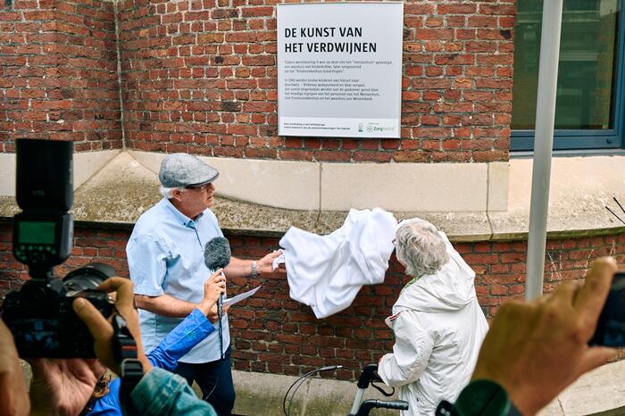 2 mensen met doek bij plakkaat op gevel.
